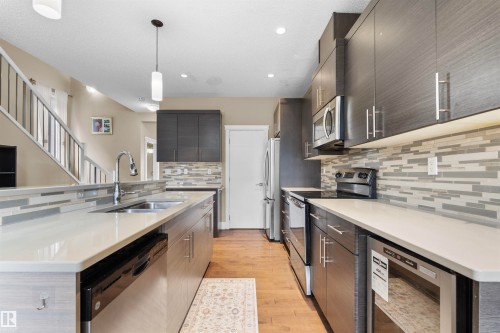 Modern kitchen featuring stainless steel appliances, dark wood-finish cabinetry, a patterned tile backsplash, light countertops, and wood-finish flooring - 11719 127 Street Nw, Edmonton, AB - Indoor Photo Showing Kitchen With Double Sink With Upgraded Kitchen