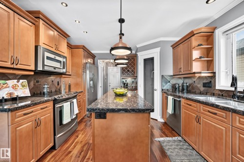 Kitchen featuring wood-finish flooring, wood cabinetry with crown molding, dark stone countertops, stainless steel appliances, and a central island with pendant lighting - 12720 Hudson Way Nw, Edmonton, AB - Indoor Photo Showing Kitchen With Double Sink With Upgraded Kitchen