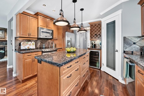 Kitchen featuring wood-finish flooring, an island with stone countertops, wood cabinetry, stainless steel appliances, and pendant lighting - 12720 Hudson Way Nw, Edmonton, AB - Indoor Photo Showing Kitchen With Upgraded Kitchen