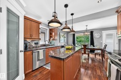 Open-concept kitchen featuring wood-finish flooring, a central island with a stone countertop, stainless steel appliances, and pendant lighting - 