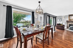 Dining area featuring wood-finish flooring, a contemporary chandelier, and a large window overlooking a body of water with distant structures - 
