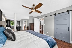 Bedroom featuring wood-finish flooring, a contemporary ceiling fan, and a light gray barn door with black hardware - 