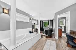 Built-in soaking tub with white tile surround, recessed wall lighting, wood-finish flooring, and a fireplace feature - 