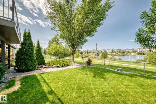Grassed backyard featuring mature trees, established landscaping, and a chain-link fence bordering a paved pathway and a body of water - 12720 Hudson Way Nw, Edmonton, AB - Outdoor With View