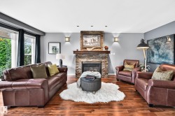 Living area featuring wood-finish flooring, a stacked stone fireplace with a wood mantel, and large windows - 