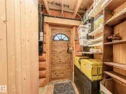 Interior space featuring a wooden plank door with an arched window, log wall construction, and exposed wood ceiling joists - 