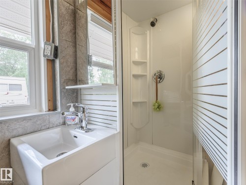 Compact bathroom featuring a white porcelain sink with chrome faucet, tiled backsplash, and a window for natural light - 58227 Range Rd 70 A, Rural St. Paul County, AB - Indoor Photo Showing Bathroom