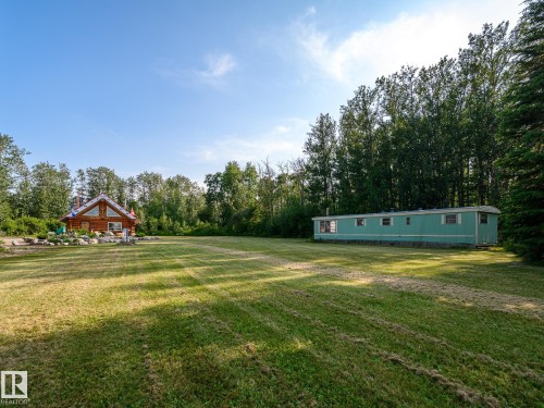 Expansive grassy area with a log cabin structure featuring a peaked roof and multiple windows, alongside a separate detached structure with light blue siding - 58227 Range Rd 70 A, Rural St. Paul County, AB - Outdoor