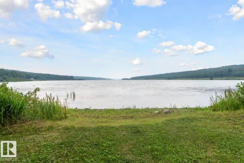 Expansive waterfrontage featuring a natural shoreline, mature trees lining the distant banks, and a clear sky with scattered clouds - 58227 Range Rd 70 A, Rural St. Paul County, AB - Outdoor With Body Of Water With View