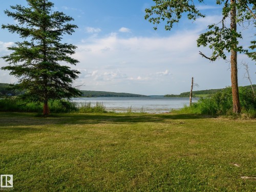 Expansive lawn area presenting a natural landscape with mature trees and waterfront access - 58227 Range Rd 70 A, Rural St. Paul County, AB - Outdoor With Body Of Water With View