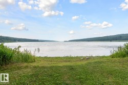 Expansive waterfrontage featuring a natural shoreline, mature trees lining the distant banks, and a clear sky with scattered clouds - 