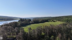 Expansive natural landscape featuring a river, mature trees, and open green fields - 