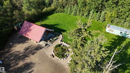 Red metal roof structure with wood siding, surrounded by mature trees, a manicured lawn, and natural landscaping - 58227 Range Rd 70 A, Rural St. Paul County, AB - Outdoor
