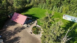Red metal roof structure with wood siding, surrounded by mature trees, a manicured lawn, and natural landscaping - 