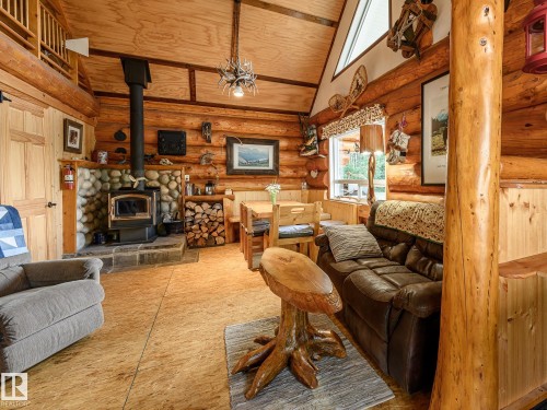 Interior log construction featuring a wood-burning stove with stone surround, natural wood-finish flooring, exposed wood beams, and an open loft area - 58227 Range Rd 70 A, Rural St. Paul County, AB - Indoor Photo Showing Living Room With Fireplace