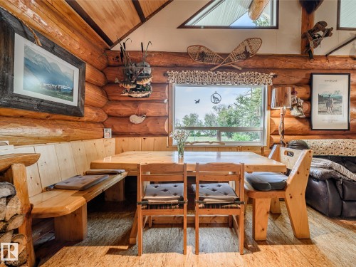 Log cabin interior featuring exposed log walls, a built-in wooden dining nook, wood-finish flooring, a large picture window, and vaulted ceilings with upper windows - 58227 Range Rd 70 A, Rural St. Paul County, AB - Indoor Photo Showing Dining Room