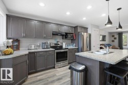 Kitchen featuring gray cabinetry, stainless steel appliances, speckled stone countertops, and wood-finish flooring - 
