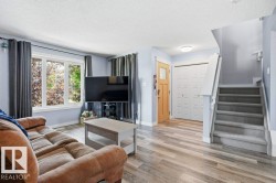 Spacious living area featuring wood-finish flooring, a large multi-pane window, and a light wood-tone entry door with frosted glass insert - 