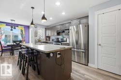 Kitchen featuring a large central island with a light-toned countertop, stainless steel appliances, grey cabinetry, and wood-finish flooring - 
