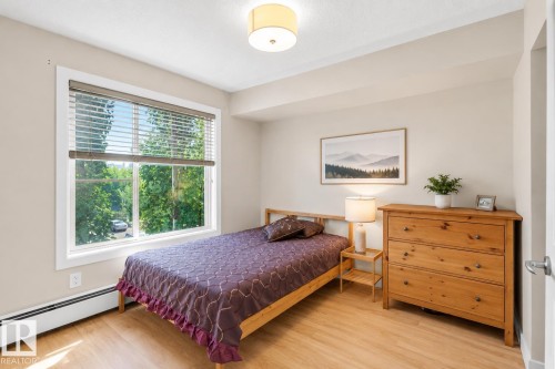 Expansive window providing abundant natural light, wood-finish flooring, overhead drum light fixture, and neutral wall tones - #317 3719 Whitelaw Ln Nw, Edmonton, AB - Indoor Photo Showing Bedroom