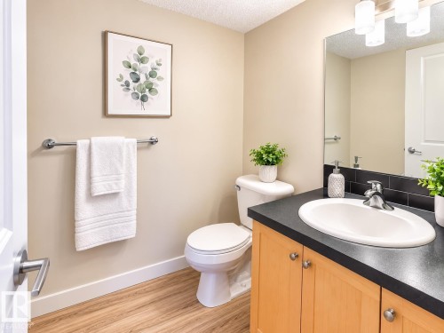 Bathroom featuring wood-finish flooring, a light wood vanity with a dark countertop and integrated sink, a large mirror, and a wall-mounted light fixture - #317 3719 Whitelaw Ln Nw, Edmonton, AB - Indoor Photo Showing Bathroom