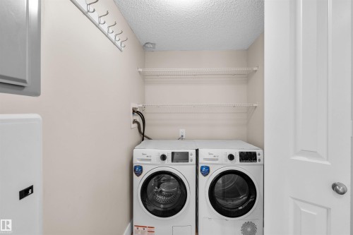Dedicated laundry area featuring a front-load washer and dryer set, two elevated wire shelves, and a wall-mounted coat rack - #317 3719 Whitelaw Ln Nw, Edmonton, AB - Indoor Photo Showing Laundry Room