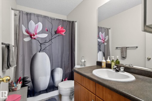 Bathroom featuring a vanity with an oval sink, dark countertop, and wood-finish cabinetry - 423 2430 Guardian Road, Edmonton, AB - Indoor Photo Showing Bathroom
