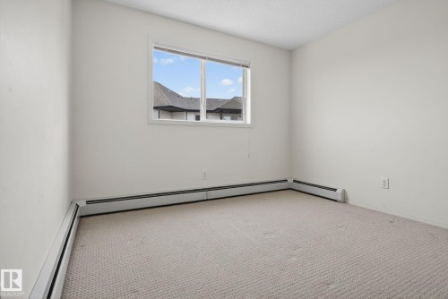 Bright room featuring neutral wall paint, light-colored patterned carpet, a large window, and baseboard heating units - 423 2430 Guardian Road, Edmonton, AB - Indoor Photo Showing Other Room