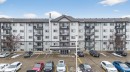 Multi-story residential building featuring balconies with black railings, a central entrance with signage, and a dedicated parking area - 423 2430 Guardian Road, Edmonton, AB  - Outdoor With Balcony With Facade 