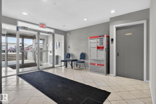 Building entry featuring large glass doors, light-toned tile flooring, recessed ceiling lighting, and a mail delivery system - 423 2430 Guardian Road, Edmonton, AB - Indoor Photo Showing Gym Room
