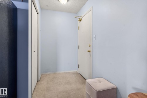 Entryway with light blue walls, beige carpet, and a white door featuring brass hardware - 423 2430 Guardian Road, Edmonton, AB - Indoor Photo Showing Other Room