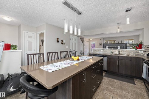 Contemporary kitchen featuring a large island with a solid surface countertop, dark wood-finish cabinetry, stainless steel appliances, a mosaic tile backsplash, and recessed lighting - 4688 Crabapple Run Sw, Edmonton, AB - Indoor Photo Showing Kitchen