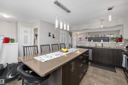 Contemporary kitchen featuring a large island with a solid surface countertop, dark wood-finish cabinetry, stainless steel appliances, a mosaic tile backsplash, and recessed lighting - 