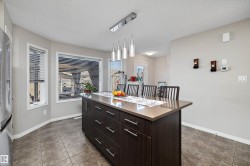 Kitchen island featuring a stone-finish countertop, dark wood-finish cabinetry, and contemporary pendant lighting - 