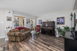 Spacious living area featuring wood-finish flooring, light grey wall tones, and multiple windows with blinds - 