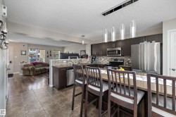 Open-concept kitchen and living area featuring dark wood-finish cabinetry, stainless steel appliances, a tile backsplash, and a breakfast bar island with pendant lighting - 