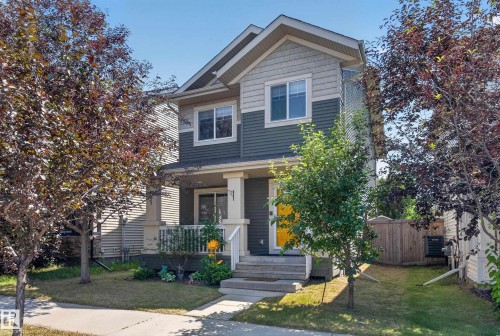 Two-story residence featuring light gray shingle siding, dark green horizontal siding, a covered front porch with white railings, and a bright yellow front door - 3139 Carpenter Landing Sw, Edmonton, AB - Outdoor