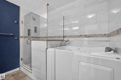 Walk-in tub with multiple jets, glass-enclosed shower, wall-mounted shower head, recessed shower niches, and decorative tile accent band - 3139 Carpenter Landing Sw, Edmonton, AB - Indoor