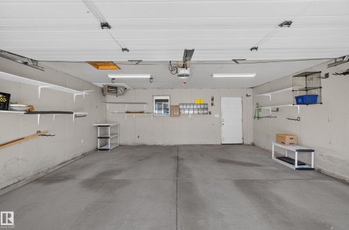 Spacious garage with concrete flooring, overhead fluorescent lighting, multiple wall-mounted shelves, and an interior access door - 3139 Carpenter Landing Sw, Edmonton, AB - Indoor Photo Showing Garage