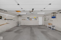 Spacious garage with concrete flooring, overhead fluorescent lighting, multiple wall-mounted shelves, and an interior access door - 