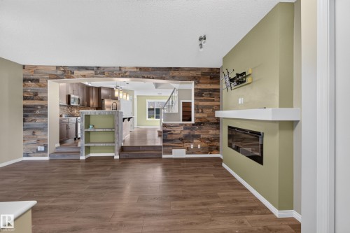 Spacious living area featuring wood-finish flooring, a contemporary fireplace with a white mantel, and a prominent accent wall crafted from varied wood planks - 3139 Carpenter Landing Sw, Edmonton, AB - Indoor With Fireplace