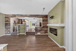 Spacious living area featuring wood-finish flooring, a contemporary fireplace with a white mantel, and a prominent accent wall crafted from varied wood planks - 