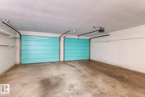 Two turquoise sectional garage doors within an interior garage space featuring a concrete floor and white painted walls - 12134 96 Street, Edmonton, AB - Indoor Photo Showing Garage