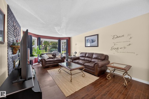 Living area featuring rich wood-finish flooring, a prominent black brick-style accent wall, and a curved bay window - 8310 99 Avenue, Fort Saskatchewan, AB - Indoor Photo Showing Living Room