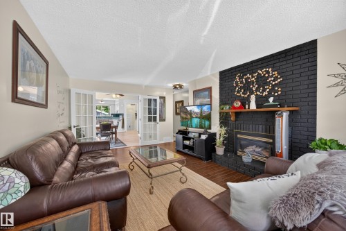 Living room featuring a dark brick fireplace with a wood mantle, wood-finish flooring, and light-toned walls - 8310 99 Avenue, Fort Saskatchewan, AB - Indoor Photo Showing Living Room With Fireplace