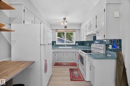 Kitchen featuring white cabinetry with brushed nickel hardware, a built-in electric range, a double-basin sink, and teal countertops with a matching tile backsplash - 8310 99 Avenue, Fort Saskatchewan, AB - Indoor Photo Showing Kitchen