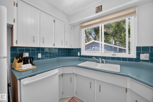 Kitchen featuring white upper and lower cabinetry, a double basin sink, and a blue tile backsplash - 8310 99 Avenue, Fort Saskatchewan, AB - Indoor Photo Showing Kitchen