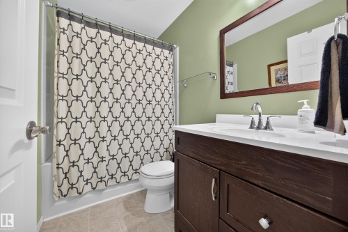 Bathroom featuring a dark wood-finish vanity with a white countertop and integrated sink, a large wood-framed mirror, and a white toilet - 8310 99 Avenue, Fort Saskatchewan, AB - Indoor Photo Showing Bathroom