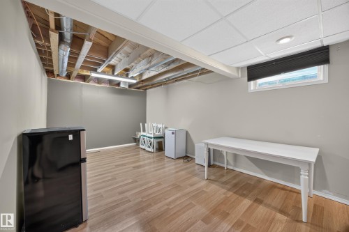 Spacious lower level room featuring wood-finish flooring, a drop ceiling with recessed lighting, and a window with a dark blind - 8310 99 Avenue, Fort Saskatchewan, AB - Indoor