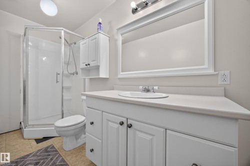 Bright bathroom featuring a corner shower enclosure, white vanity with integrated sink, framed mirror, and coordinating wall-mounted storage cabinet - 8310 99 Avenue, Fort Saskatchewan, AB - Indoor Photo Showing Bathroom